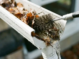 Gootborstel ruimt bladeren en puin uit witte dakgoot terwijl helder water doorstroomt bij daglicht